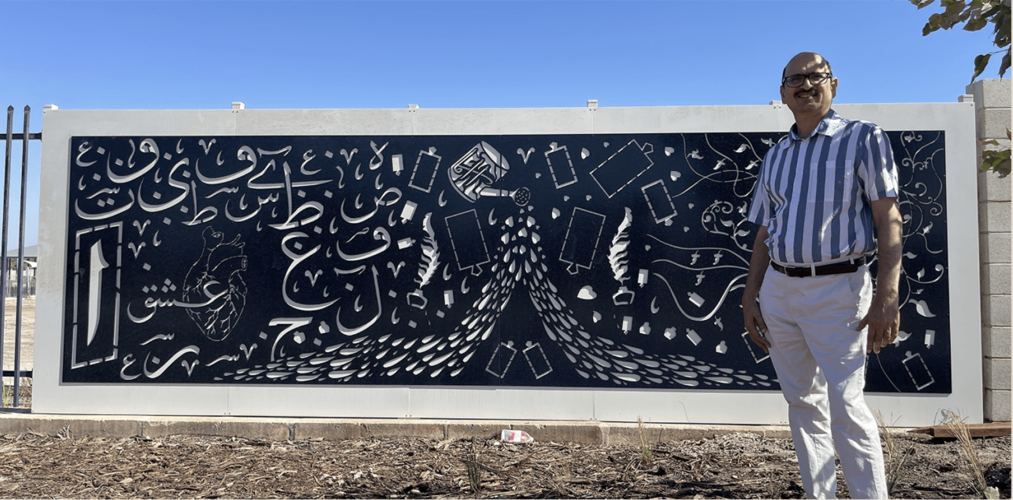 Tusif Ahmad standing beside a large custom Islamic paper-cut mural artwork